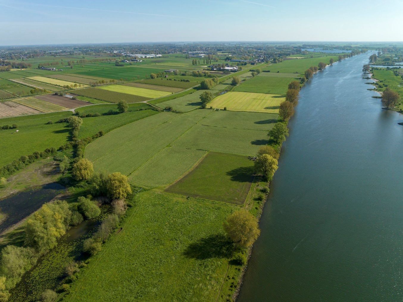 Gebied Casterens Hoeve Oever vanuit de lucht gezien. Dit is een oeverstrook langs de Maas die bestaat uit grasland en bomen en rechts grenst aan de Maas.